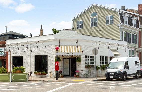 Front view of a two-story building with a white brick facade and striped awnings over the windows.