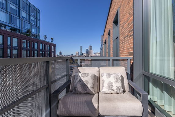 Balcony with outdoor seating offering a view of surrounding buildings and skyline.