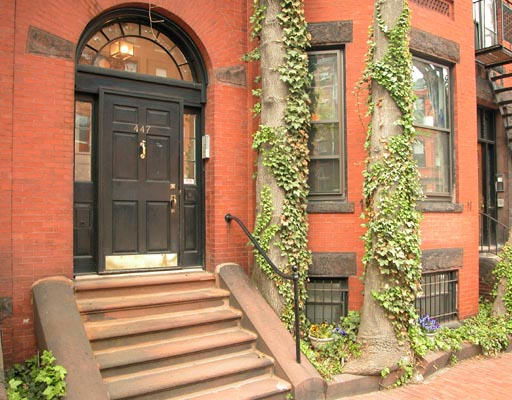 Front view of a brick building with a black door and steps leading up to the entrance.