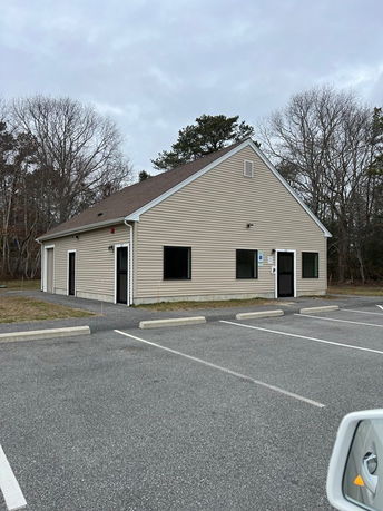 Front view of a small, single-story building with a gable roof and beige siding.