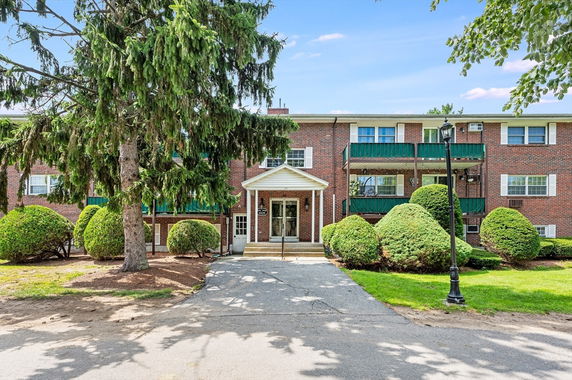 Front view of a brick residential building with green balconies and entrance.