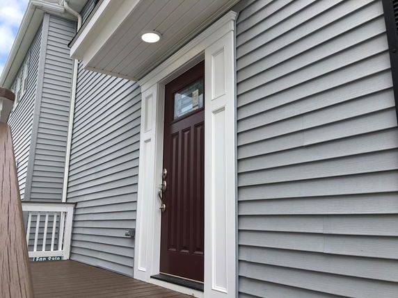 Side view of a house entrance with a dark wooden door and grey siding.
