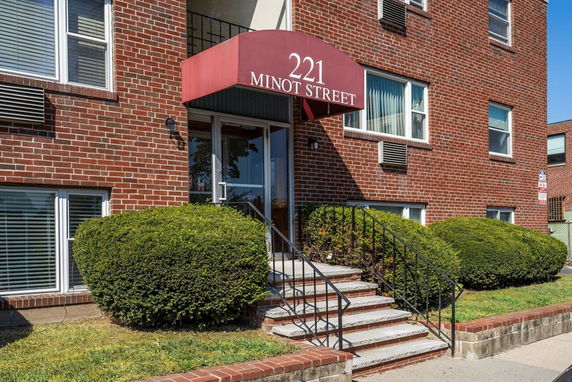Front view of a multi-story brick apartment building with a red awning over the entrance.