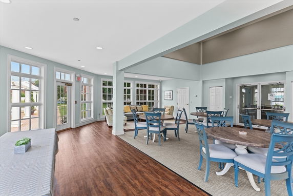 Interior view of a clubhouse with tables and chairs, wooden flooring, and large windows.
