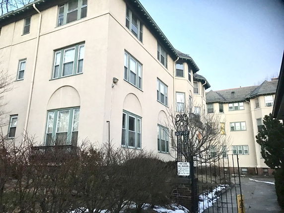 Front view of a multi-story apartment building with numerous windows and an entrance gate.