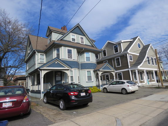 Front view of two adjacent multi-story houses with parking spaces.