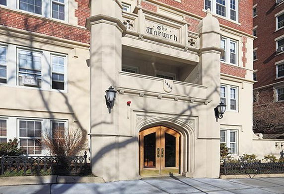 Front view of an apartment building with an arched entrance and brick facade.