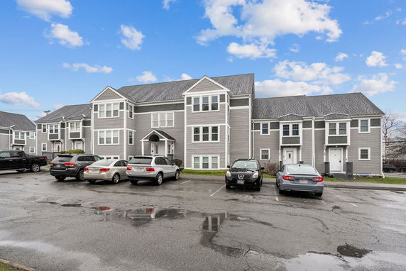 Front view of a multi-story apartment building with gray siding and several parked cars in front.