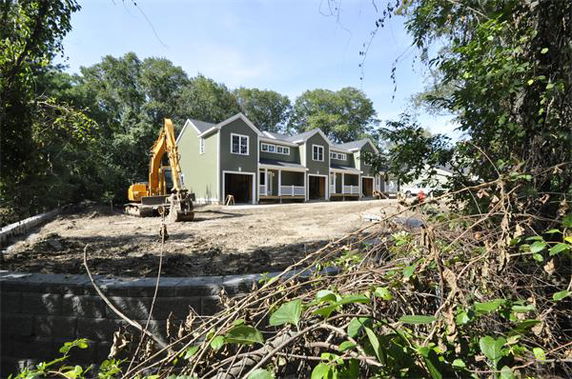 Front view of a row of three newly constructed townhouses with gabled roofs.