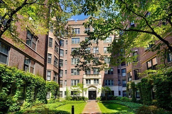 Front view of a multi-story brick building with an entrance and surrounding greenery.