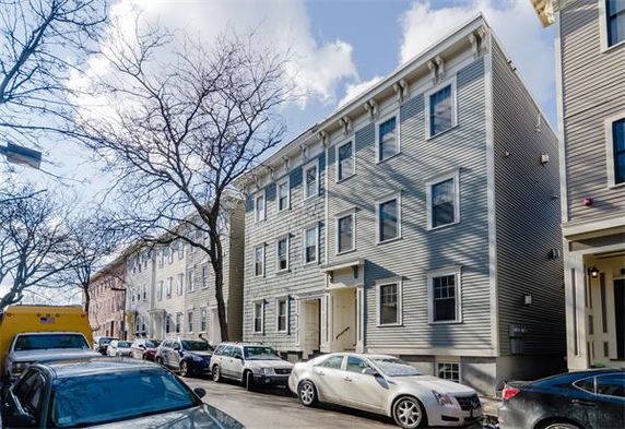Front view of a multi-story residential building with cars parked in front.
