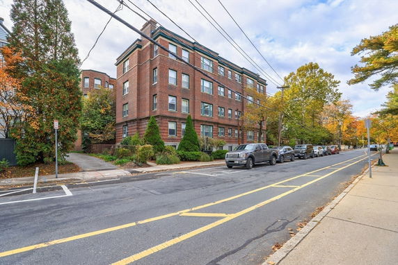 Front view of a multi-story brick apartment building on a tree-lined street.