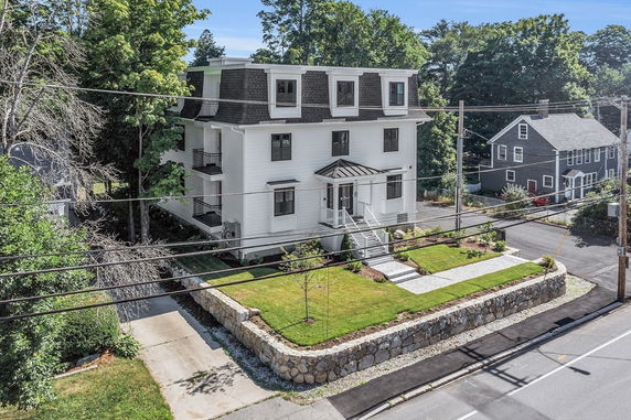 Front view of a multi-story house with manicured lawn and stone retaining wall.