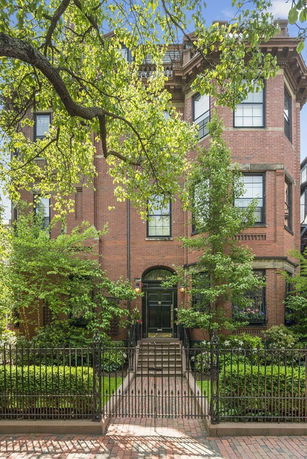 Front view of a multi-story brick house with a black iron fence.