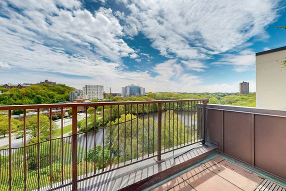 Panoramic view from a rooftop showing a cityscape and greenery under a cloudy sky.