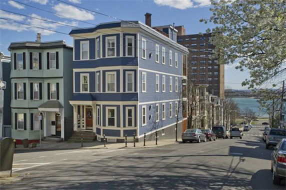 Front view of a blue multi-story residential building on a street corner.
