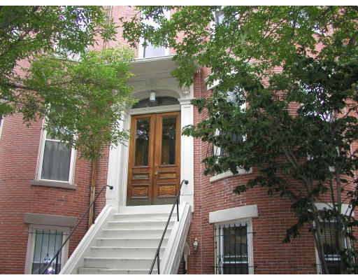 Front view of a brick building with a staircase and wooden door entrance.
