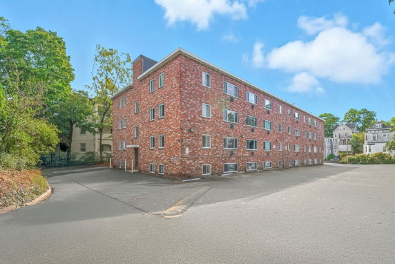Front view of a multi-story brick building with multiple windows and an entrance on the side.