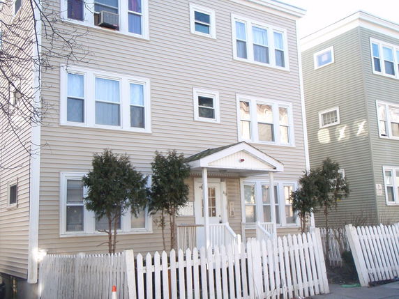 Front view of a three-story house with a white picket fence.