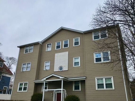 Front view of a multi-story residential building with a sloped roof and multiple windows.