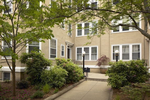 Front view of a multi-story residential building with a garden and a pathway leading to the entrance.
