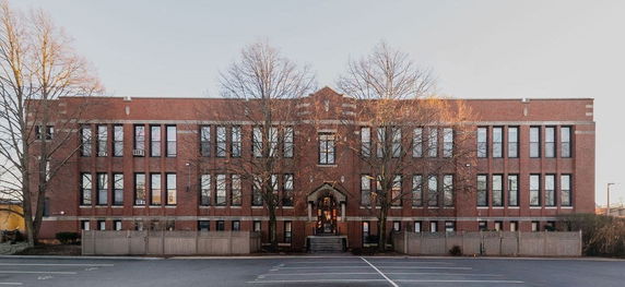 Front view of a multi-story brick building with large windows and an entrance with stairs.