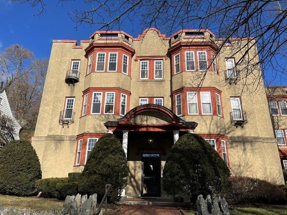 Front view of a multi-story building with red trim and bay windows.