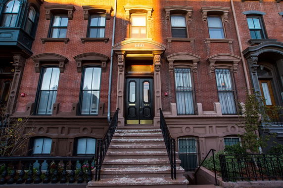 Front view of a multi-story brick townhouse with ornate window frames and a central staircase leading to the entrance.