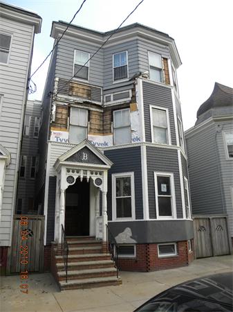 Front view of a three-story house with light blue siding and a small porch with stairs.