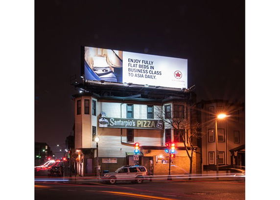 Nighttime street view of a building with a pizza restaurant on the ground floor and a large illuminated billboard on the roof.