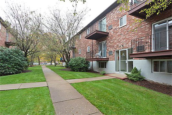 Front view of a multi-story brick apartment building with balconies and pathway.