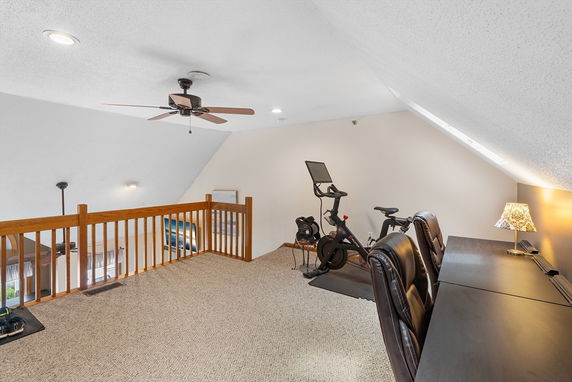 Interior view of a home gym and workspace area with exercise bike and desk with chairs.