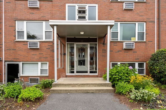 Front view of a multi-story brick apartment building with multiple windows and air conditioning units.