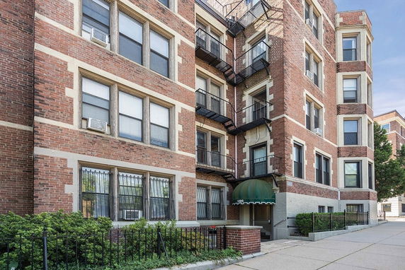 Front view of a multi-story brick apartment building with fire escapes.
