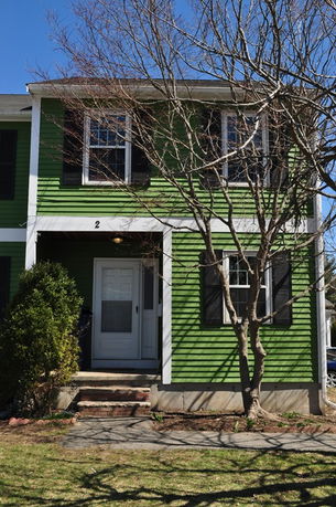 Front view of a green two-story house with black shutters and a white door.