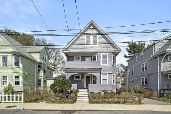 Front view of a three-story house with a steep gable roof and a porch.