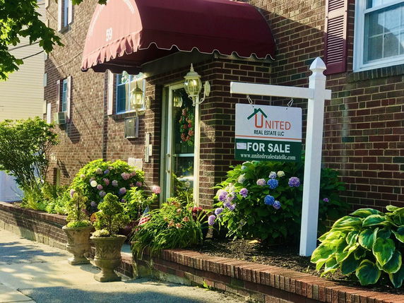 Front view of a brick building with an awning and a real estate for sale sign.