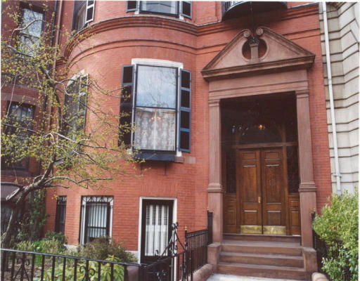 Front view of a brick residential building with a curved facade and large wooden door.