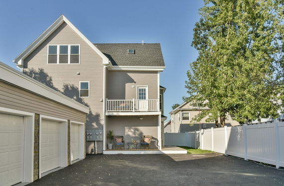 Rear view of a multi-story house with a balcony and an adjacent garage.