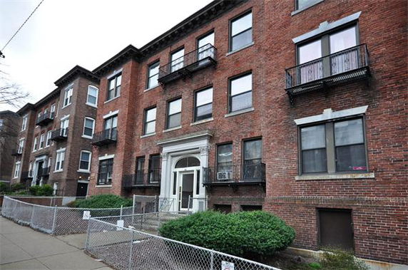 Front view of a multi-story brick apartment building with multiple windows and small balconies.