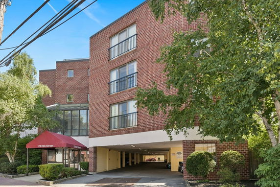 Front view of a multi-story brick building with large windows and an entrance under a red awning.
