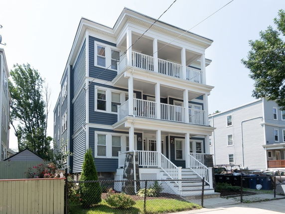 Front view of a three-story residential building with balconies and a fenced yard.