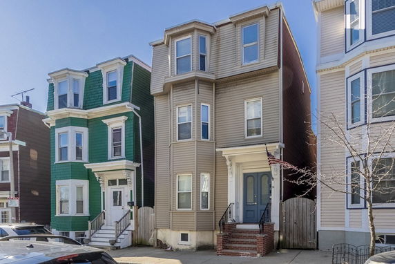 Front view of a multi-story townhouse with beige siding and blue door.