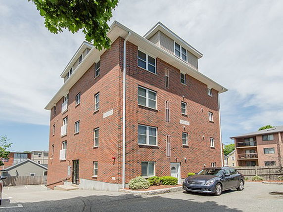 Front view of a multi-story brick apartment building with parking area.