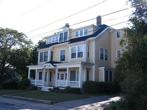 Front view of a multi-story yellow house with a porch and chimney.