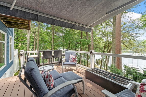 Deck area attached to a house with seating and a view of trees and water.
