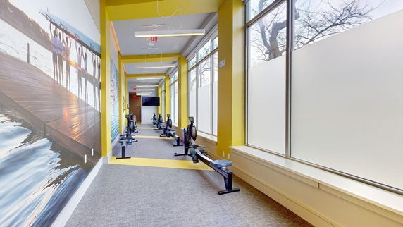 Indoor gym area with rowing machines and large windows.