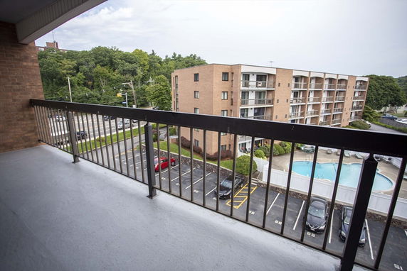 View from a balcony overlooking a multi-story building with a swimming pool and parking area.