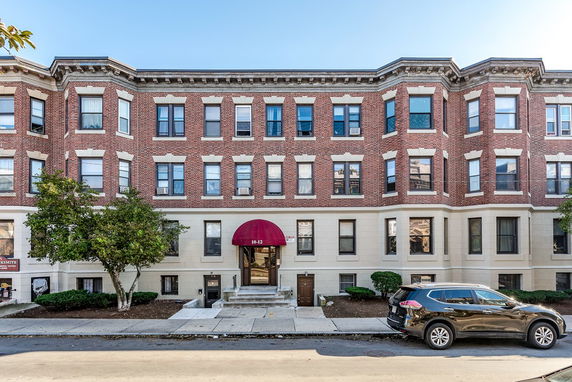Front view of a multi-story brick apartment building with a central entrance and bay windows.