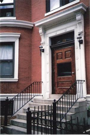 Front view of a brick building entrance with steps and wrought iron railings.
